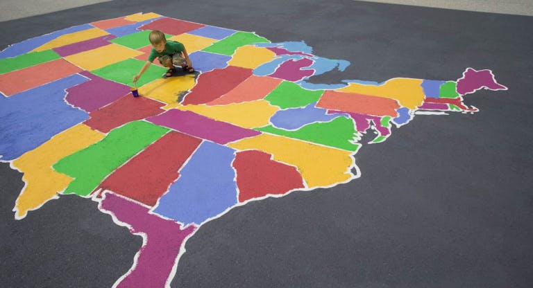 Boy (5-7) painting map of USA in playground, outdoors