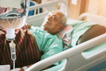 An elderly man with an IV lies in a hospital bed