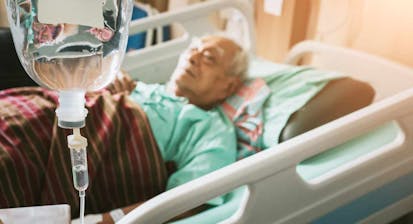 An elderly man with an IV lies in a hospital bed
