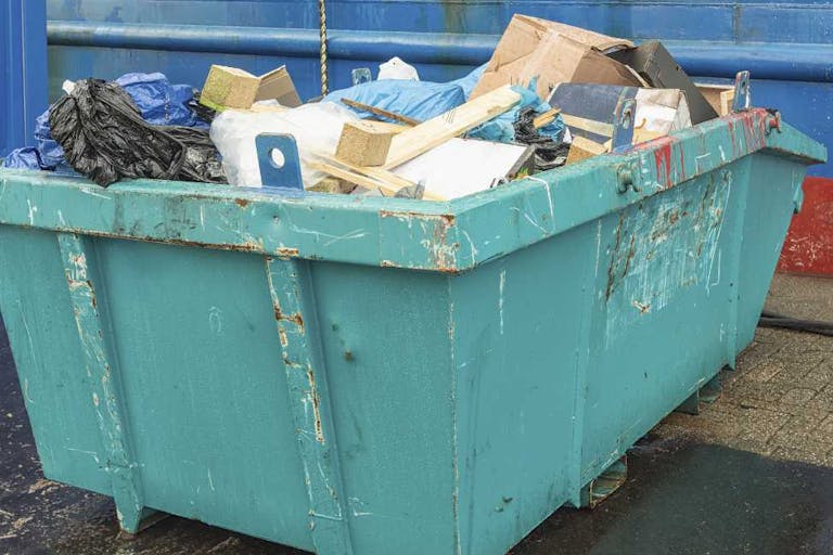 open green steel industrial waste container filled with various waste