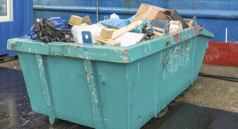 open green steel industrial waste container filled with various waste