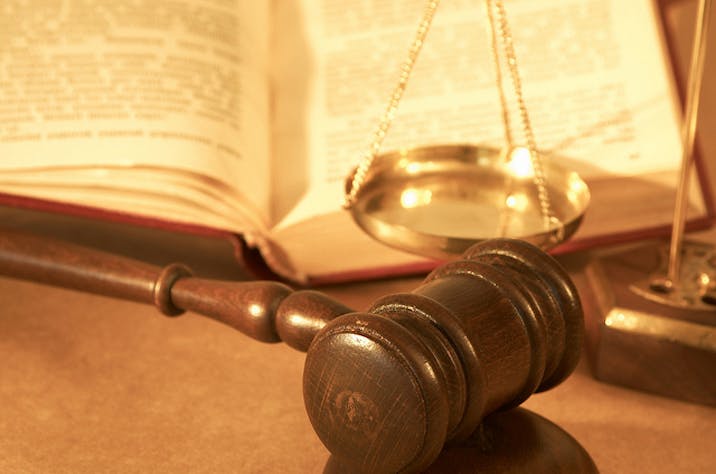 A gavel sits on a table in front of an open book and a scale.