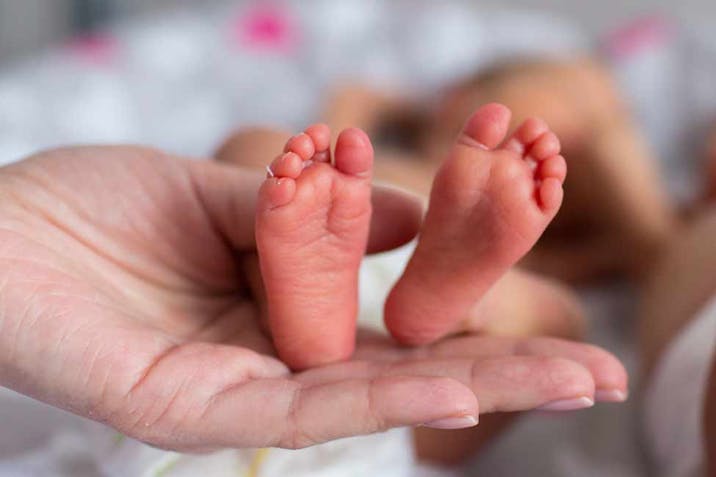 A woman's hand holding the feet of a premature baby.
