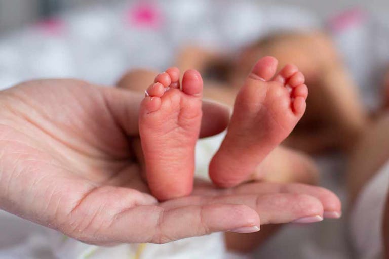 A woman's hand holding the feet of a premature baby.