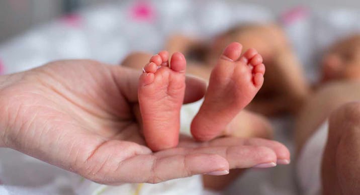 A woman's hand holding the feet of a premature baby.