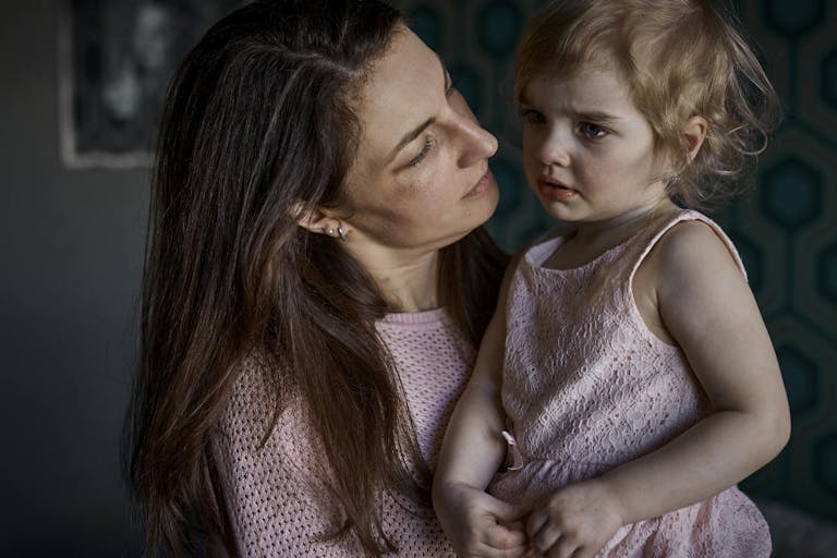 Mother consoling sad toddler girl at home