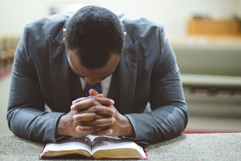 Lonely african-american male praying with his hands on the Bible with his head down