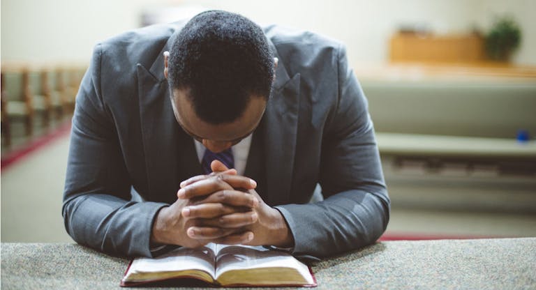 Lonely african-american male praying with his hands on the Bible with his head down