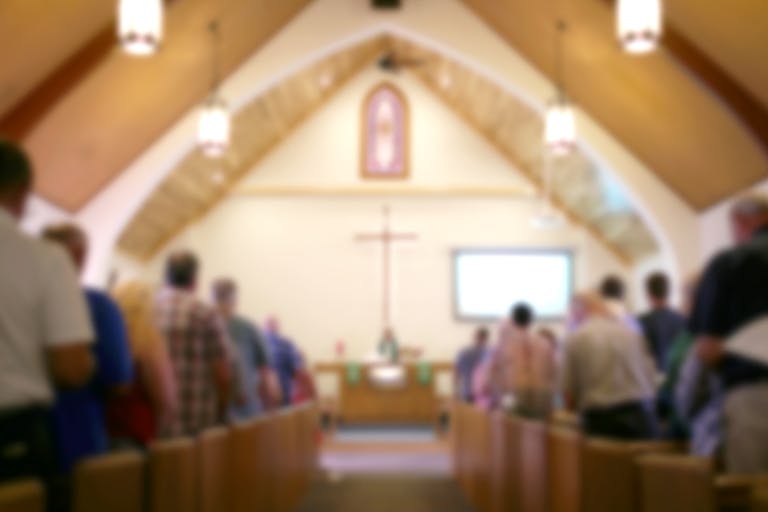 Blurred Photo of the Iterior of a Church Sanctuary with Congregation, Pastor, and a Large Cross Visible