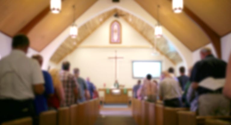 Blurred Photo of the Iterior of a Church Sanctuary with Congregation, Pastor, and a Large Cross Visible