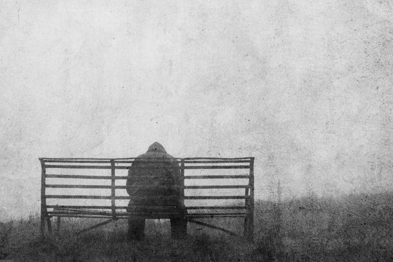 A mental health concept of mysterious figure back to camera, sitting on a bench alone. With a grunge, textured edit.