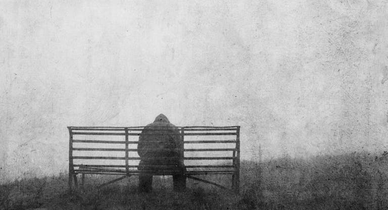 A mental health concept of mysterious figure back to camera,  sitting on a bench alone. With a grunge, textured edit.