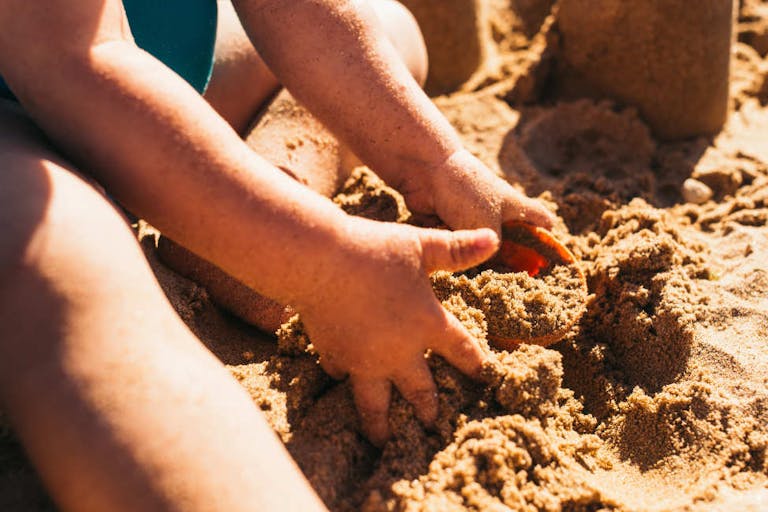 Toddler girl playing with a bucket in the sand of a beach.