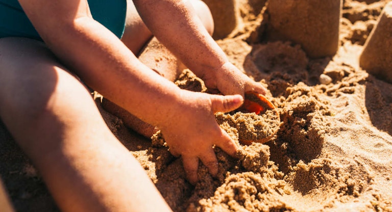 Toddler girl playing with a bucket in the sand of a beach.
