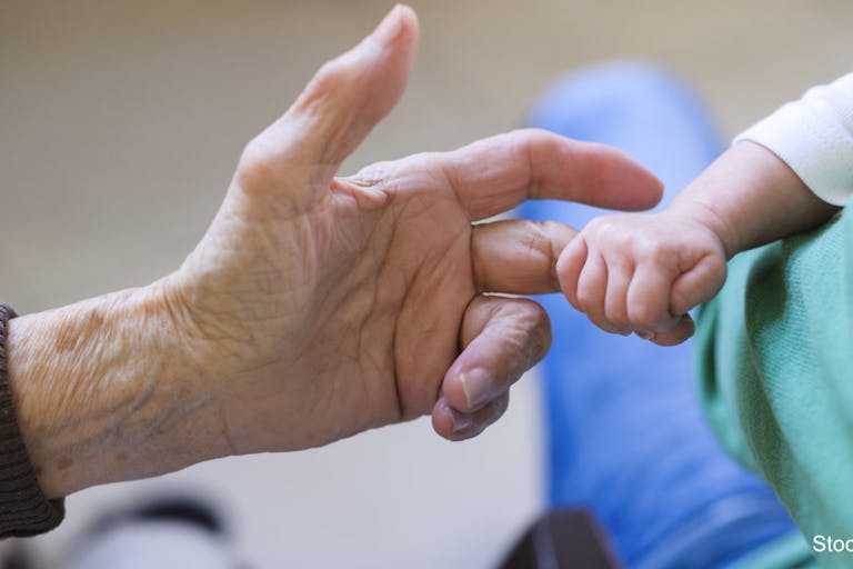 Baby holding finger of her great grandmother’s hand