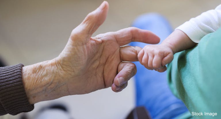 Baby holding finger of her great grandmother’s hand