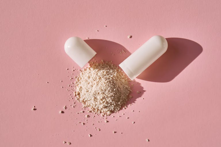 An open capsule with its contents on a pink background.