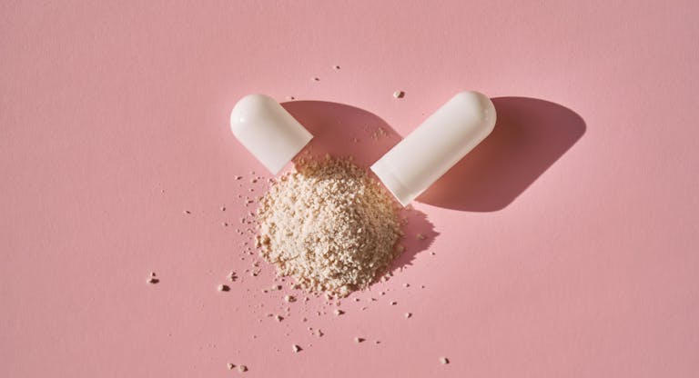 An open capsule with its contents on a pink background.