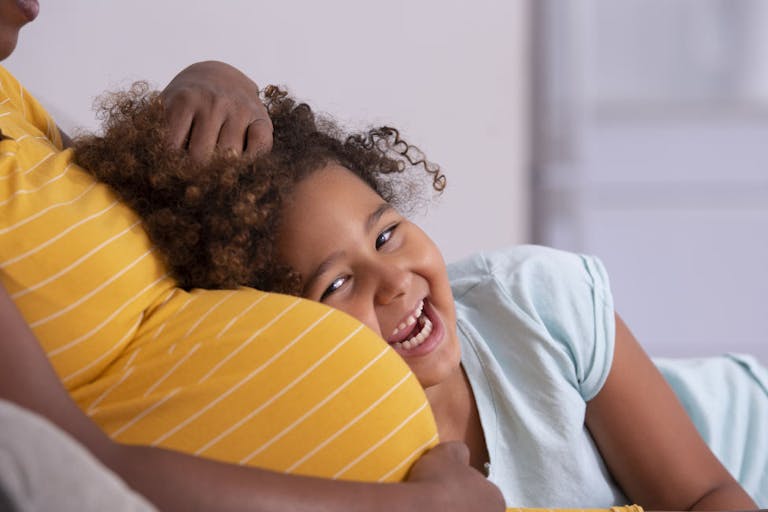 Happy little mixed-race girl leaning against pregnant mother’s belly.