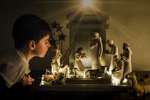 Young boy leaning in looking closely at a ceramic nativity scene.