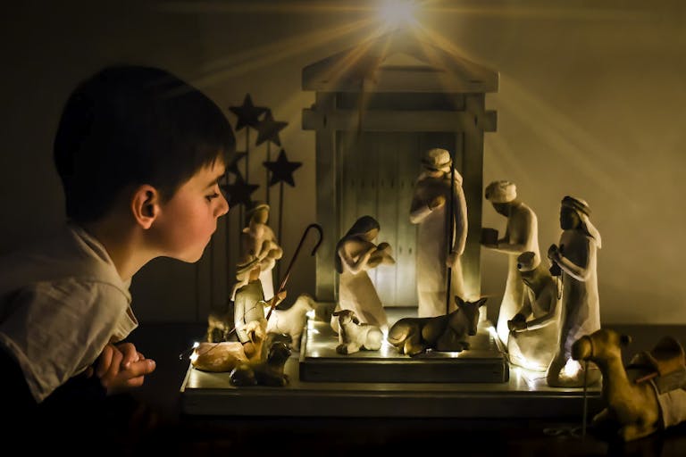 Young boy leaning in looking closely at a ceramic nativity scene.