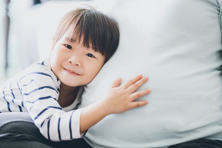 Photo: Getty Images Cute little Asian girl touching and listening to pregnant mother’s belly with joy