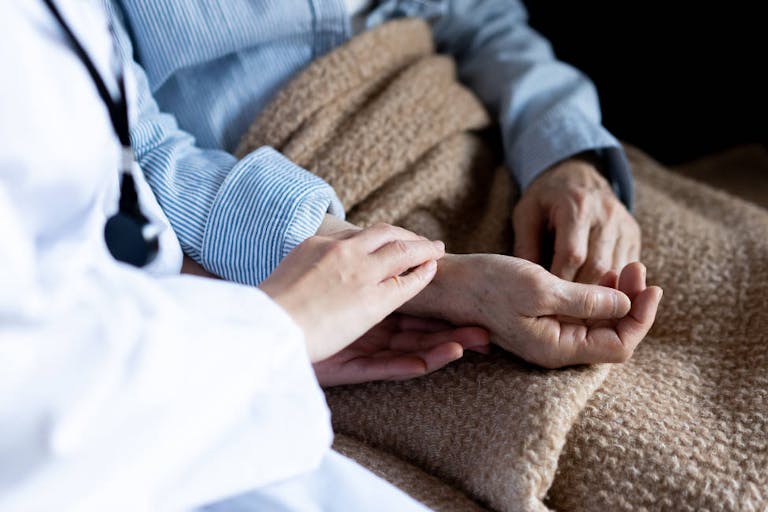 Photo: Getty Images photo of person in white lab coat holding arm of person in bed