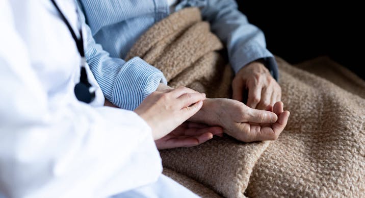 photo of person in white lab coat holding arm of person in bed