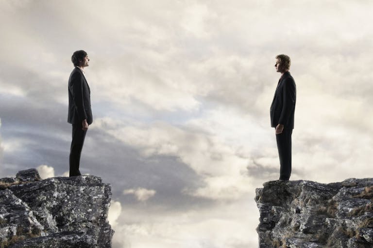 Businessmen looking at each other across chasm