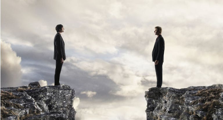Businessmen looking at each other across chasm
