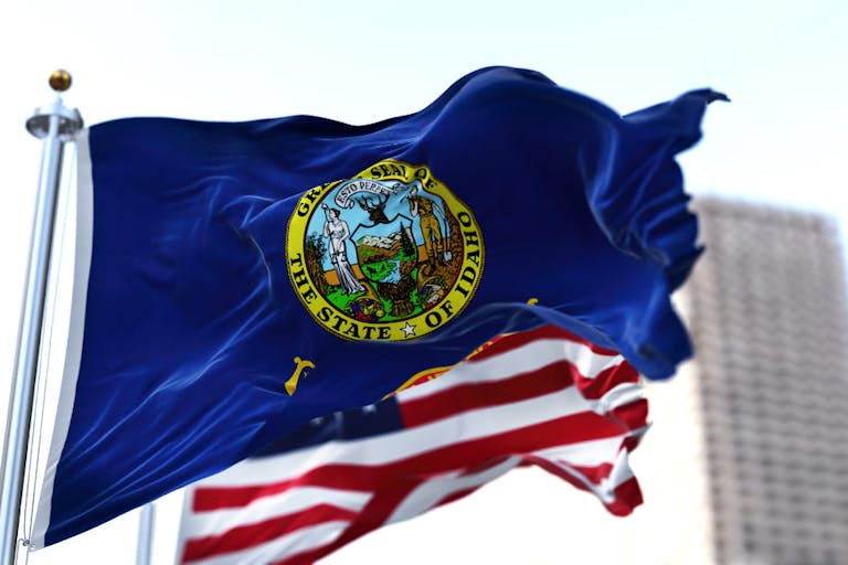 the flag of the US state of Idaho waving in the wind with the American stars and stripes flag blurred in the background
