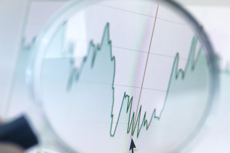Investor analysing line graph on computer screen with magnifying glass