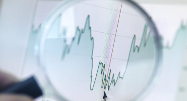 Investor analysing line graph on computer screen with magnifying glass