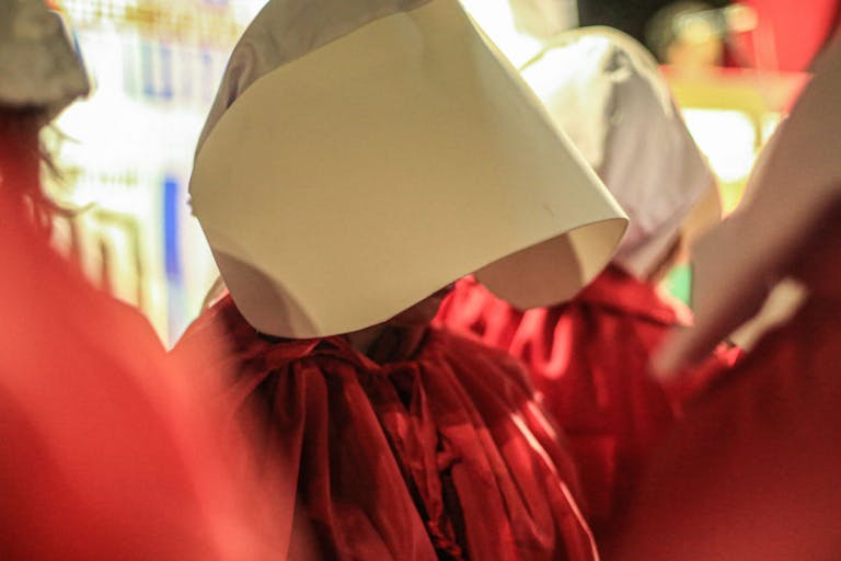 Female protesters wear red robes and bonnets representing