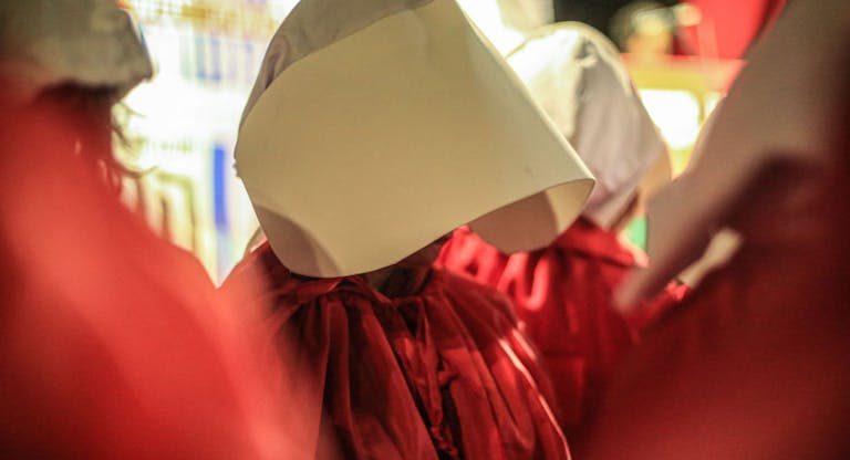 Female protesters wear red robes and bonnets representing