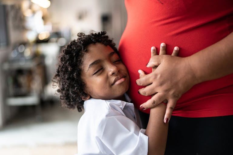 Young son putting hand on pregnant mothers stomach at home