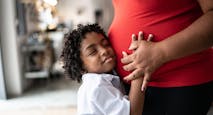 Young son putting hand on pregnant mothers stomach at home