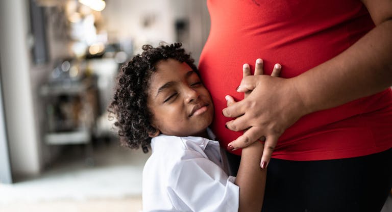 Young son putting hand on pregnant mothers stomach at home