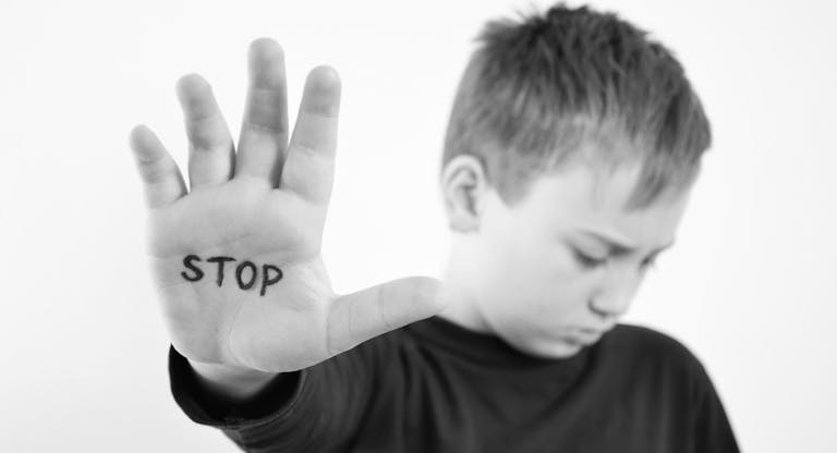 Small abused boy holding his hand with the word ‘STOP’ written on it.