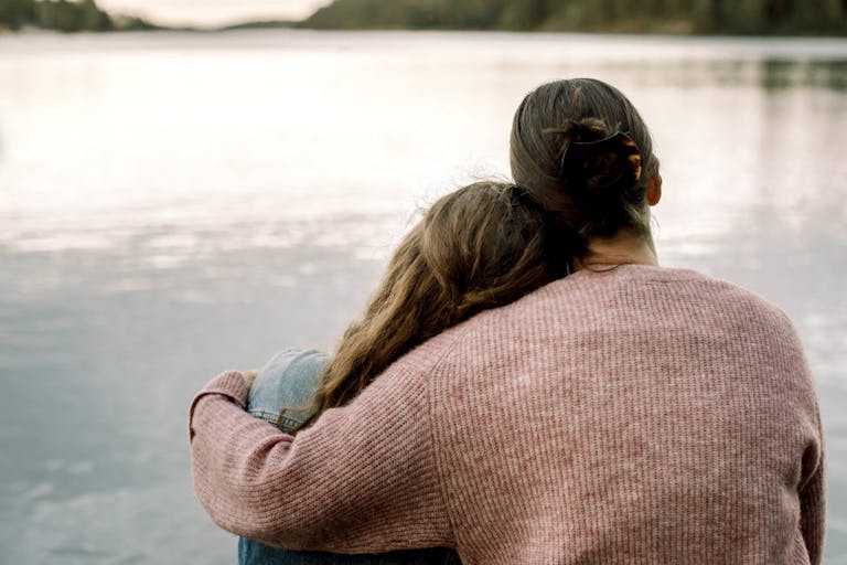 Rear view of mother with daughter sitting by lake