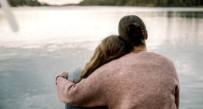 Rear view of mother with daughter sitting by lake