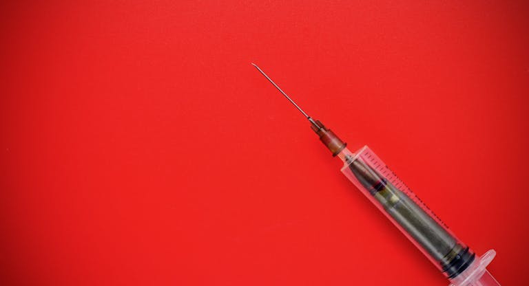Bullet in a disposable syringe on a red background