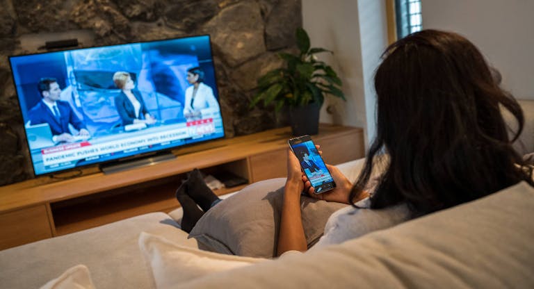 Woman sitting in living room and watching news broadcast