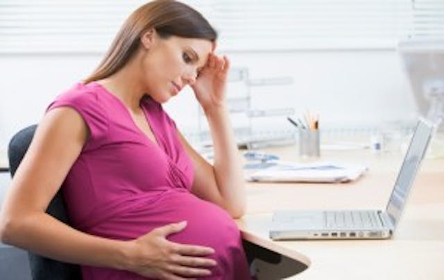 Pregnant woman at work with laptop looking stressed