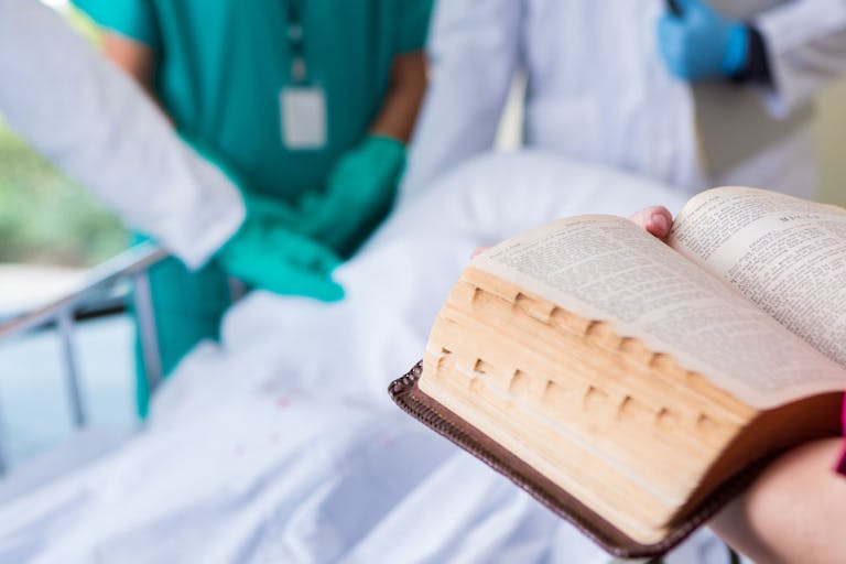 Hospital nurse or chaplain reading bible in patient room