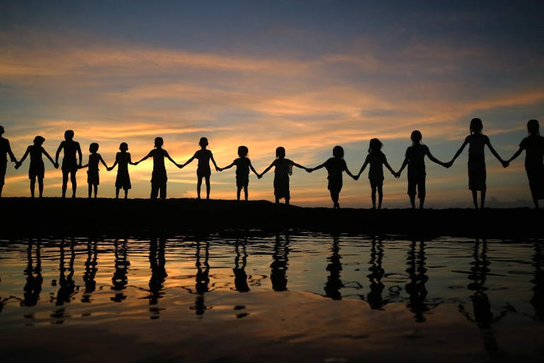 Silhouette Children Holding Hands While Standing Against Sky During Sunset