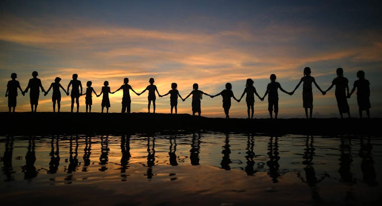 Silhouette Children Holding Hands While Standing Against Sky During Sunset