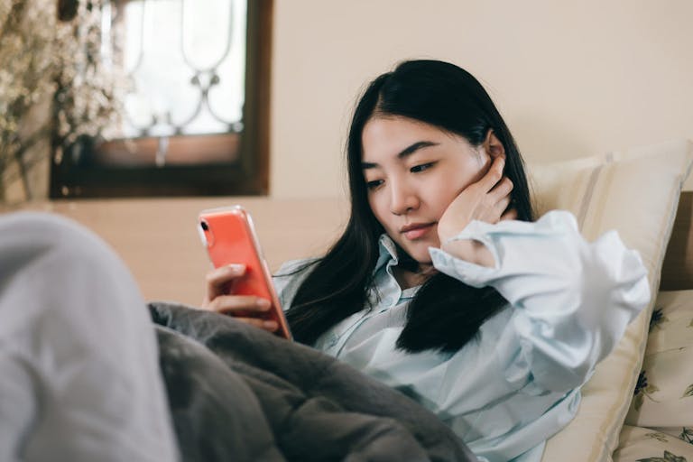 Young adult single woman using smartphone in the bed.