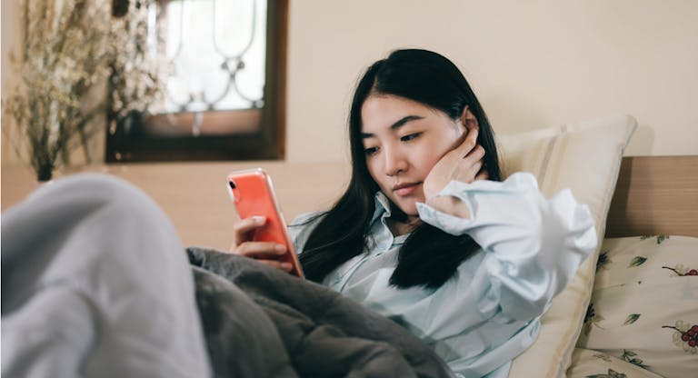 Young adult single woman using smartphone in the bed.