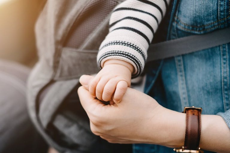 Close up of mother carrying baby and holding hand